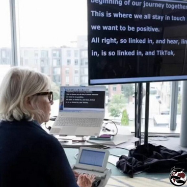 A CART writer transcribing captions using a stenograph which are displayed on large screen in the background.
