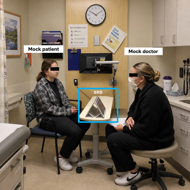 A mock patient and a mock doctor sitting across a table in a clinic room with a tablet showing real-time captions highlighted between them.